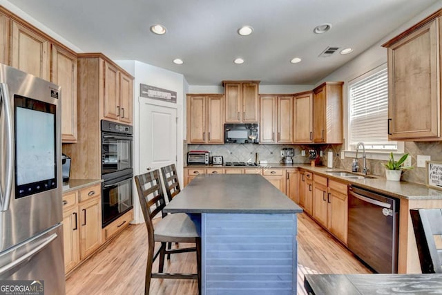 kitchen featuring backsplash, sink, black appliances, a center island, and light hardwood / wood-style floors