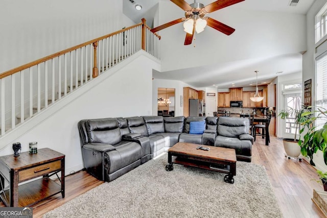 living room with ceiling fan with notable chandelier, light hardwood / wood-style floors, and high vaulted ceiling