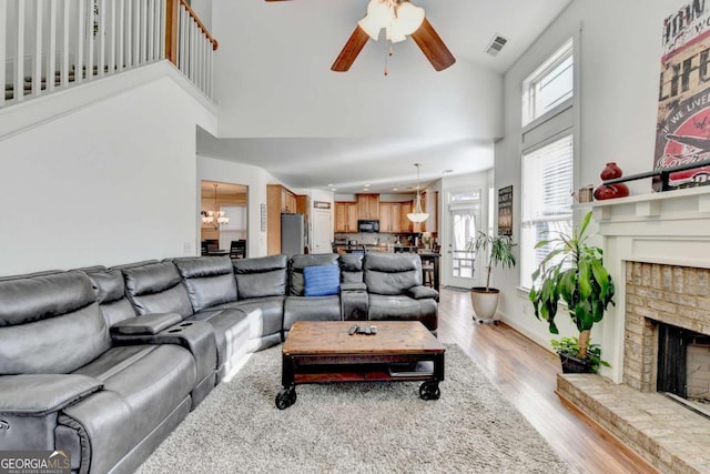 living room with ceiling fan with notable chandelier, light wood-type flooring, a fireplace, and a towering ceiling