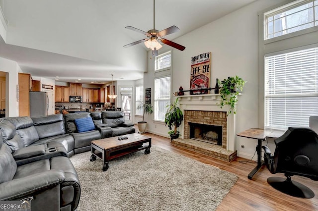 living room featuring a fireplace, a high ceiling, light hardwood / wood-style flooring, and ceiling fan