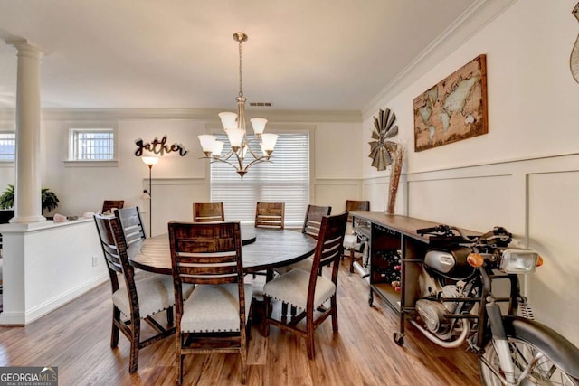 dining space featuring ornate columns, crown molding, wood-type flooring, and a notable chandelier