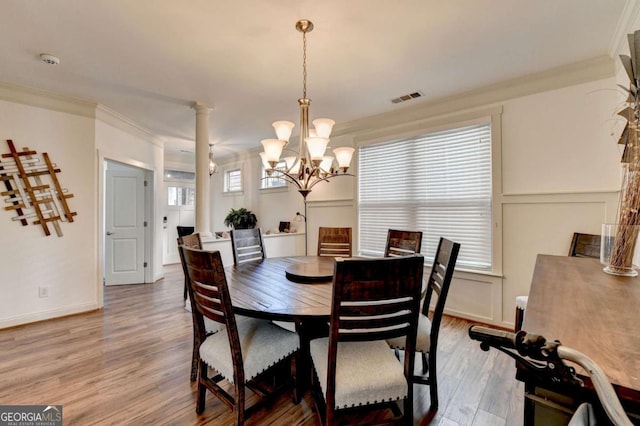 dining room with ornate columns, an inviting chandelier, ornamental molding, and hardwood / wood-style flooring