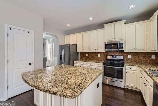 kitchen with a center island, light stone counters, dark wood-type flooring, and appliances with stainless steel finishes