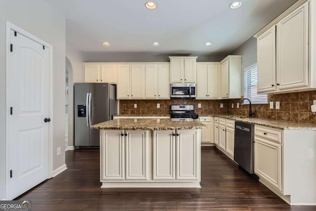 kitchen with sink, light stone counters, dark hardwood / wood-style floors, a kitchen island, and appliances with stainless steel finishes