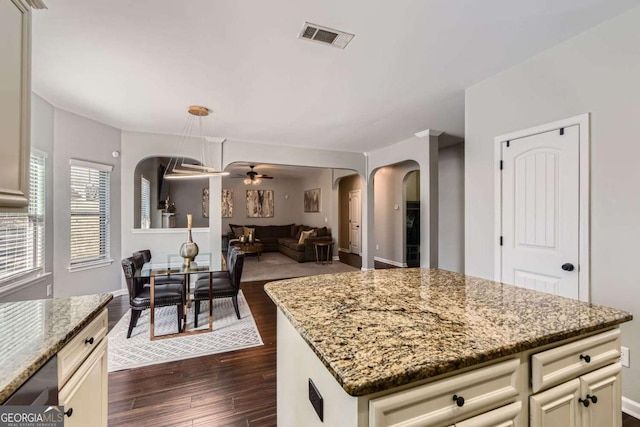 kitchen with light stone counters, ceiling fan, dark wood-type flooring, cream cabinetry, and a kitchen island