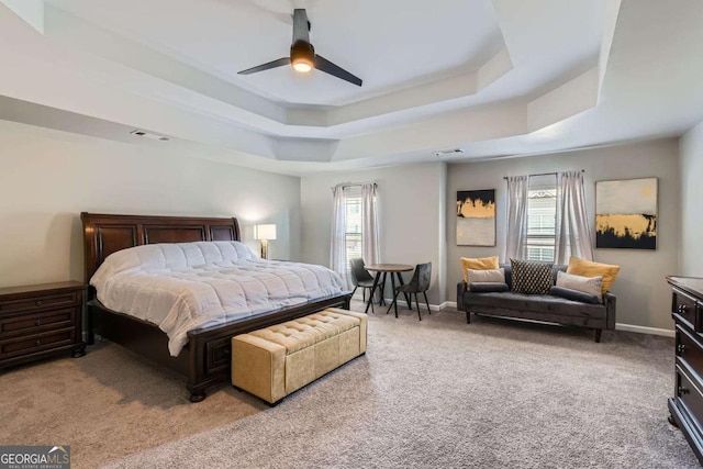 bedroom with light colored carpet, a raised ceiling, and ceiling fan