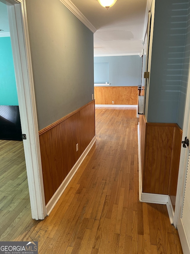 corridor with hardwood / wood-style flooring, ornamental molding, and wooden walls