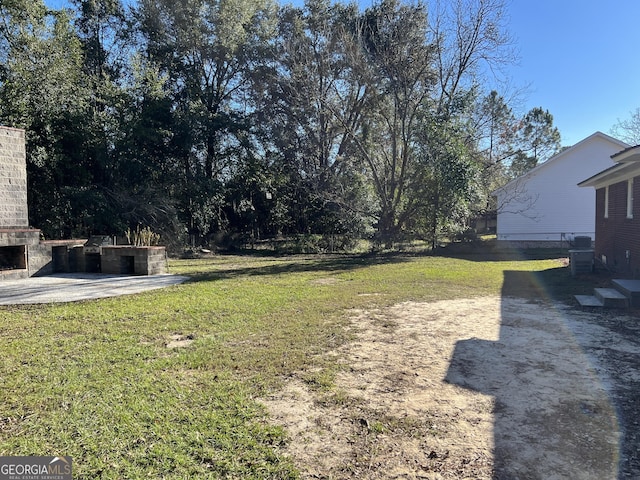 view of yard with an outdoor brick fireplace and a patio area