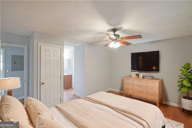 bedroom featuring ceiling fan, connected bathroom, electric panel, and light hardwood / wood-style flooring