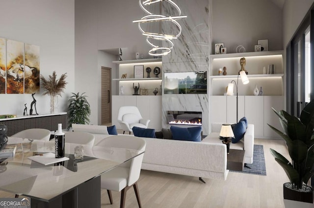 living room featuring a high end fireplace, light hardwood / wood-style floors, a high ceiling, and a notable chandelier