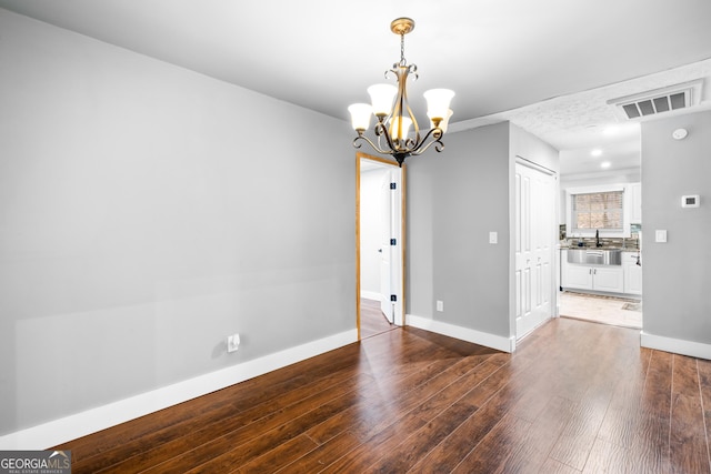 empty room featuring sink, dark wood-type flooring, and a notable chandelier