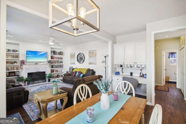 dining area featuring ceiling fan with notable chandelier, a fireplace, dark wood-type flooring, and built in shelves