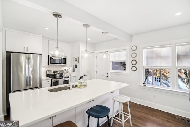 kitchen with dark hardwood / wood-style floors, pendant lighting, a breakfast bar area, white cabinets, and appliances with stainless steel finishes