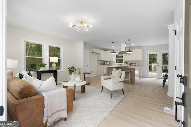 living room featuring a notable chandelier, plenty of natural light, light wood-type flooring, and french doors