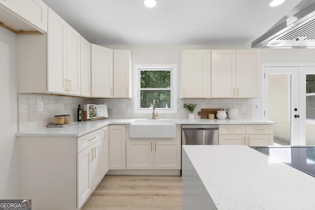 kitchen with white cabinets, sink, stainless steel dishwasher, light wood-type flooring, and range hood