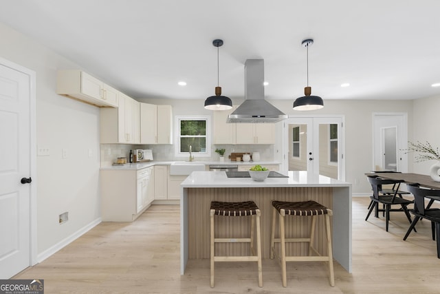 kitchen with pendant lighting, sink, light wood-type flooring, white cabinetry, and island exhaust hood