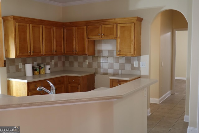 kitchen featuring sink, backsplash, kitchen peninsula, crown molding, and light tile patterned flooring