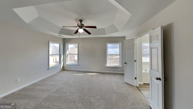 unfurnished bedroom featuring ceiling fan, a raised ceiling, and light carpet