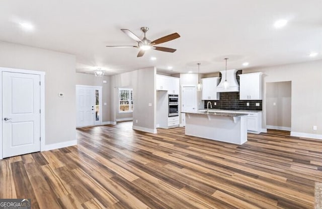 kitchen with hanging light fixtures, dark hardwood / wood-style floors, a kitchen island with sink, white cabinets, and custom range hood