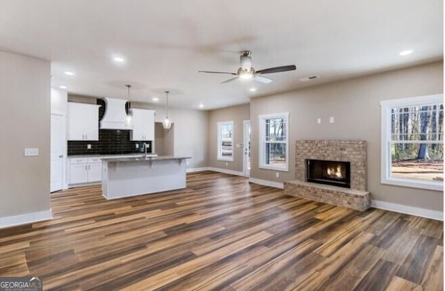 kitchen with white cabinetry, a center island with sink, dark hardwood / wood-style floors, and decorative light fixtures