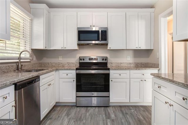 kitchen featuring light stone counters, stainless steel appliances, sink, white cabinets, and light hardwood / wood-style floors