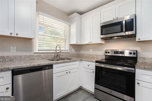 kitchen featuring white cabinets, sink, light hardwood / wood-style floors, light stone counters, and stainless steel appliances