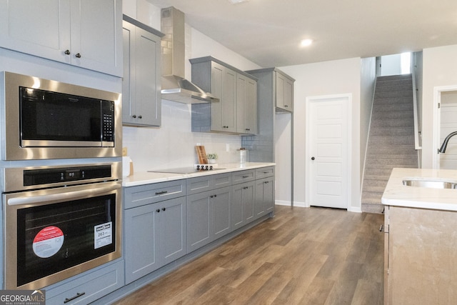 kitchen featuring wall chimney exhaust hood, built in microwave, black electric cooktop, light countertops, and a sink