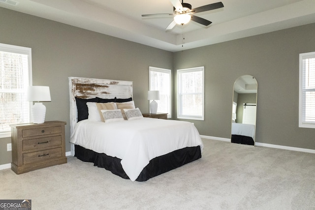 bedroom featuring light carpet, baseboards, and a raised ceiling