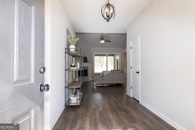 entrance foyer featuring ceiling fan with notable chandelier, dark wood-style flooring, a fireplace, and baseboards