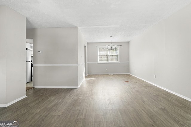 spare room featuring a chandelier, dark wood-type flooring, and a textured ceiling