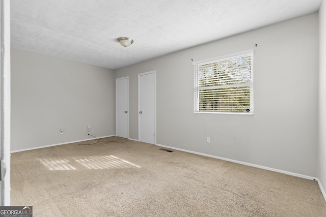 spare room featuring a textured ceiling and light colored carpet