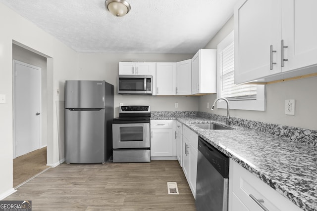 kitchen with sink, stainless steel appliances, light hardwood / wood-style floors, a textured ceiling, and white cabinets