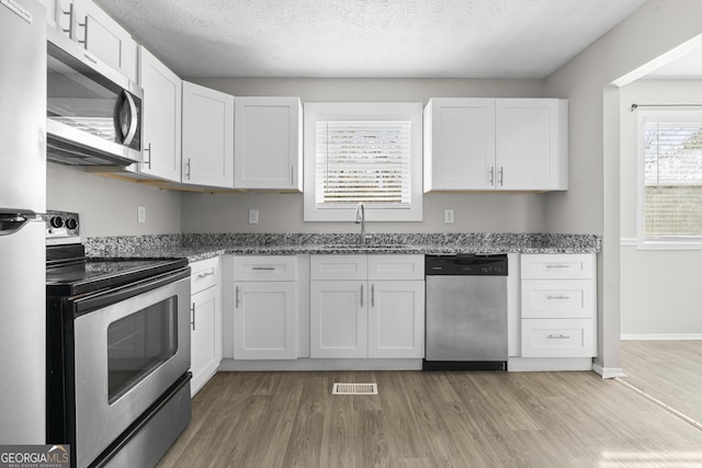 kitchen with sink, stainless steel appliances, a textured ceiling, white cabinets, and light wood-type flooring