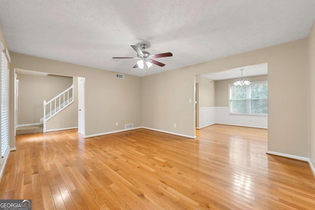 unfurnished living room featuring light hardwood / wood-style flooring, ceiling fan with notable chandelier, and a textured ceiling