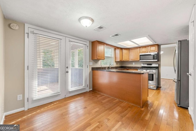 kitchen featuring kitchen peninsula, light wood-type flooring, a textured ceiling, and appliances with stainless steel finishes