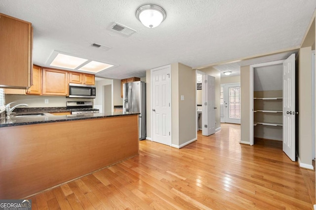 kitchen with kitchen peninsula, a textured ceiling, stainless steel appliances, sink, and light hardwood / wood-style flooring