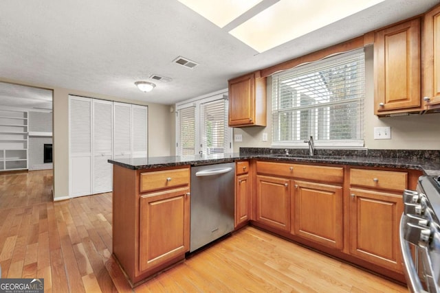 kitchen featuring sink, stainless steel appliances, dark stone counters, light hardwood / wood-style floors, and a textured ceiling