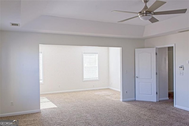 unfurnished bedroom featuring light carpet, a tray ceiling, and ceiling fan