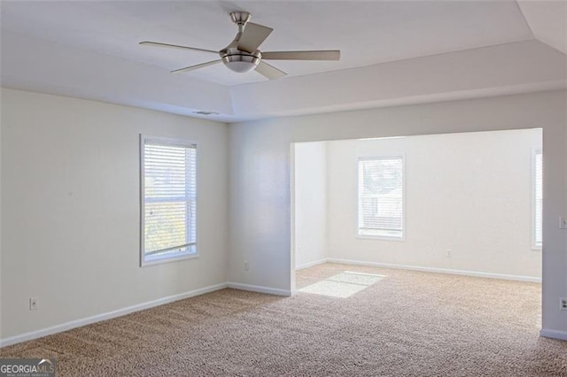 spare room featuring a raised ceiling, ceiling fan, light colored carpet, and a healthy amount of sunlight