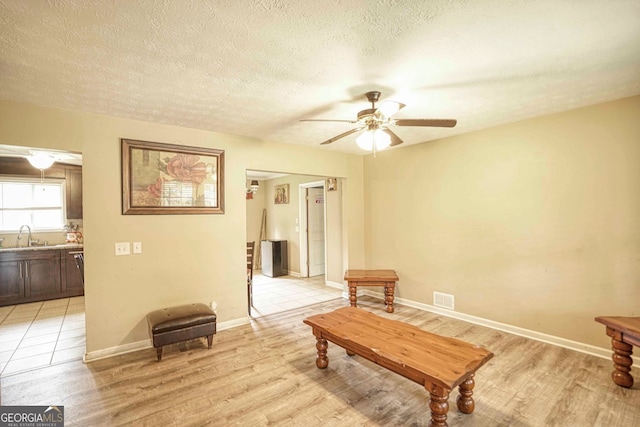 interior space featuring ceiling fan, sink, light wood-type flooring, and a textured ceiling