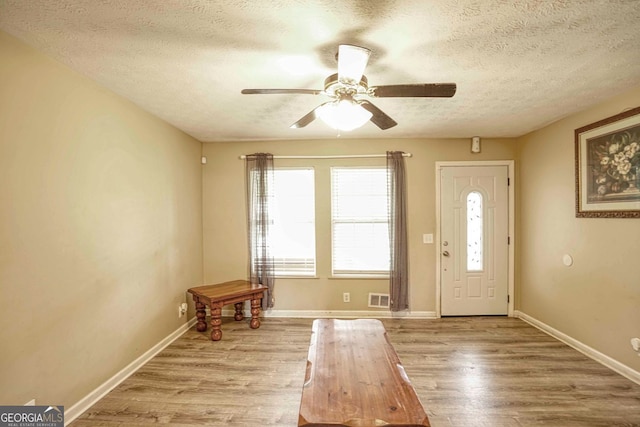 foyer entrance with ceiling fan, a textured ceiling, and light hardwood / wood-style flooring