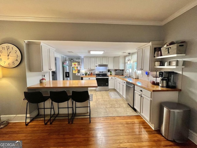 kitchen featuring kitchen peninsula, appliances with stainless steel finishes, white cabinets, light hardwood / wood-style floors, and butcher block counters