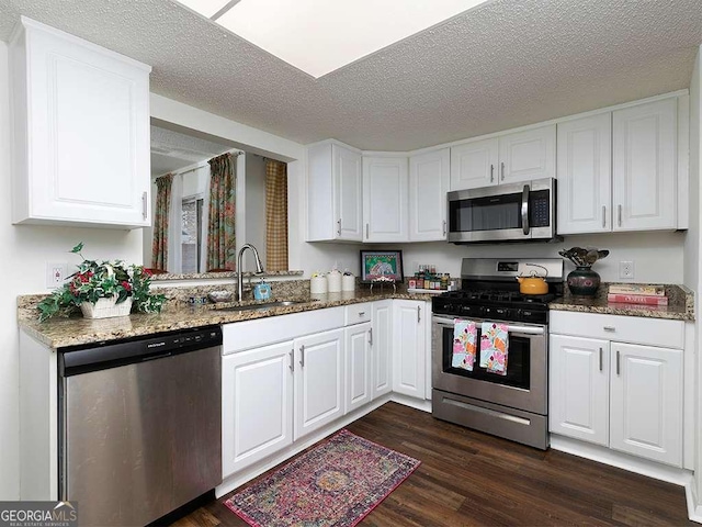 kitchen with dark hardwood / wood-style floors, dark stone counters, a textured ceiling, white cabinets, and appliances with stainless steel finishes