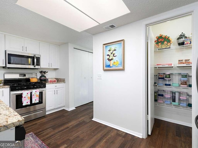 kitchen with dark wood-type flooring, light stone countertops, a textured ceiling, appliances with stainless steel finishes, and white cabinetry