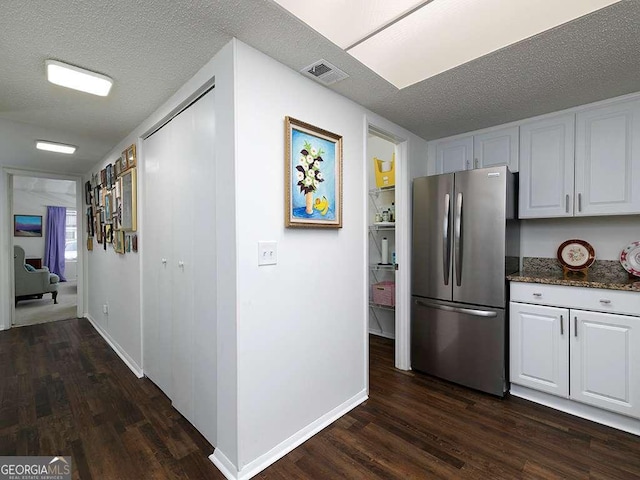 kitchen featuring dark stone counters, white cabinets, dark hardwood / wood-style floors, stainless steel fridge, and a textured ceiling