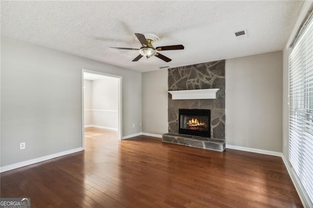 unfurnished living room with a textured ceiling, dark hardwood / wood-style floors, a stone fireplace, and ceiling fan