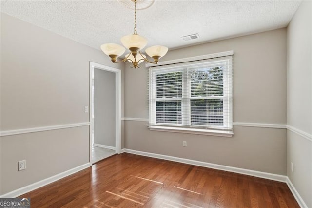 empty room featuring a chandelier, a textured ceiling, and hardwood / wood-style flooring