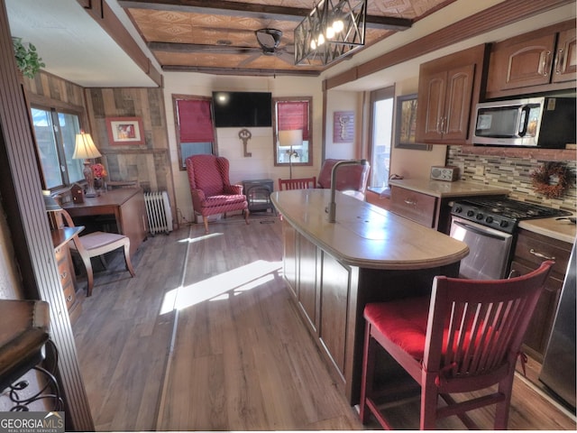 kitchen featuring radiator, ceiling fan, a kitchen island, appliances with stainless steel finishes, and light hardwood / wood-style floors