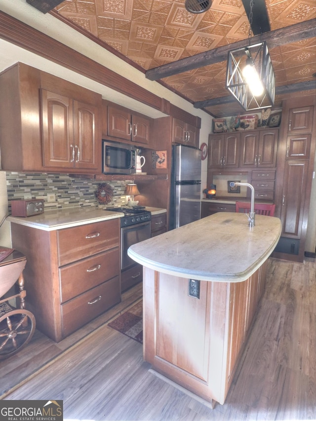 kitchen with appliances with stainless steel finishes, dark hardwood / wood-style flooring, brick ceiling, a kitchen island with sink, and pendant lighting