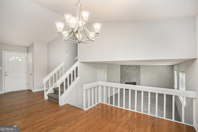 staircase with vaulted ceiling, a stone fireplace, a notable chandelier, and hardwood / wood-style flooring